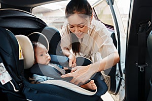 happy mother is fastening safety belt to newborn baby in car seat