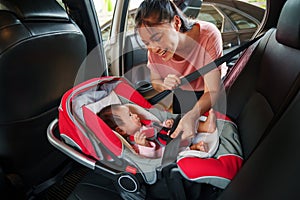 happy mother is fastening safety belt to newborn baby in car seat