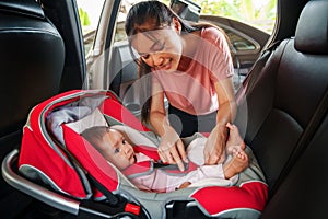 happy mother is fastening safety belt to newborn baby in car seat