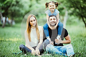 Happy mother, father and daughter in the park. Beauty nature scene with family outdoor lifestyle. Happy daughter on father back sm