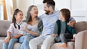 Happy mother and father hugging with children, sitting on couch