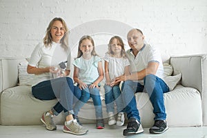 Happy mother and father with little children sitting on sofa and laughing while having fun together at home during weekend