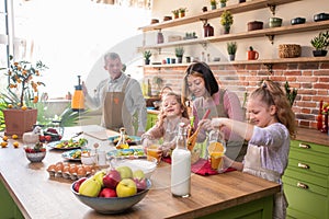 Happy mother and father with two kids baking together, standing at wooden countertop in modern kitchen, young parents