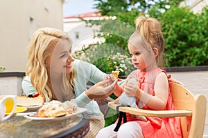 Happy mother feeding daughter with cake at cafe