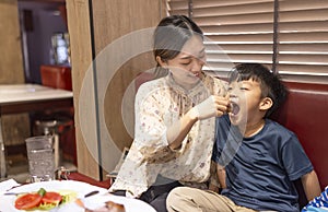 Happy mother feeds her son in restaurant