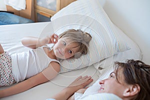 Happy mother and girl daughter waking up on bed at morning together.Happy relaxed parents enjoying life with their