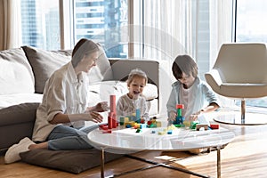Happy mother helping little sibling kids to build toy towers