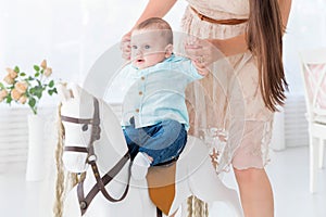 A happy mother helps a little son to mount a toy horse.