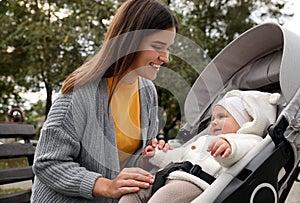 Happy mother with her adorable baby in stroller sitting on bench outdoors