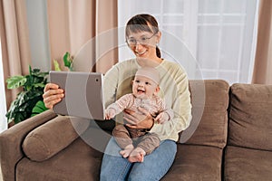 Smiling mom and her baby having video call on tablet at home