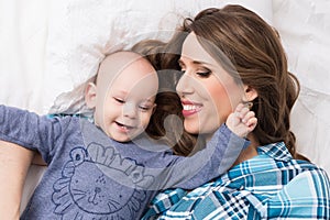 Happy mother and her baby son lying on a bed together. Happy family. Mother and newborn child.