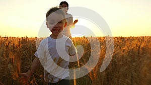 A happy mother and her child are running across a field of wheat during sunset.