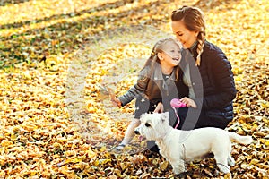 Happy mother and her daughter playing with dog in autumn park. Family, pet, domestic animal and lifestyle concept. Autumn time. Ha