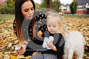 Happy mother and her daughter playing with dog in autumn park. Family, pet, domestic animal and lifestyle concept