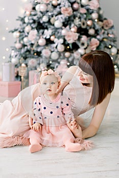 Happy mother with her daughter playing near the Christmas tree. Mother kissing and hugging her daughter. Christmas