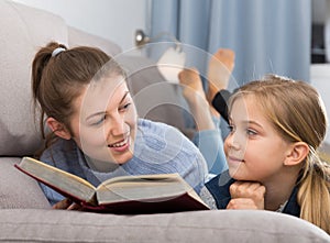 Happy mother with her daughter reading a book on the couch at home