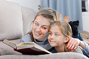 Happy mother with her daughter reading a book on the couch at home