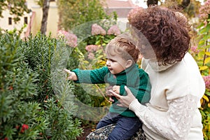 Happy mother and her little boy. Child playing with mother in the park. Mother and son embracing. Child studies a bush in the park