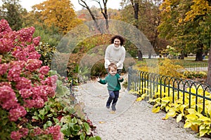 Happy mother and her little child walking in the park. Laughter mother and  son playing and runing in the garden. Autumn time
