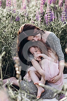 Happy mother and her little daughter in a field of lupins in summer. Mom and baby have fun