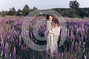 Happy mother and her little daughter in a field of lupins in summer. Mom holds her baby in arms