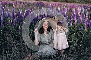 Happy mother and her little daughter in a field of lupins in summer. Mom holds her baby in arms