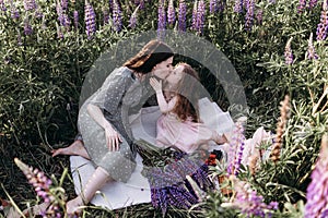 Happy mother and her little daughter in a field of lupins in summer. Mom kisses a happy baby