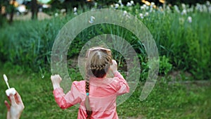 Happy Mother and her little Daughter playing together outdoor, blowing soap bubbles, having fun on backyard. Nature