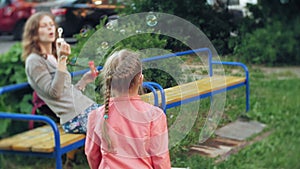 Happy Mother and her little Daughter playing together outdoor, blowing soap bubbles, having fun on backyard. Nature