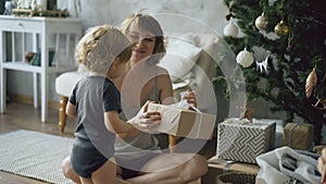 Happy mother and her little daughter unpack gift box near the Christmas tree at home