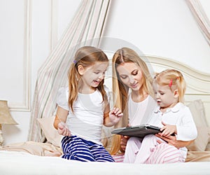 Happy mother and her little daughters having fun using a tablet