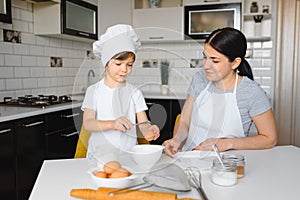 Happy mother and her little son shaking raw eggs in bowl before making dough for homemade pastry in the kitchen