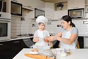 Happy mother and her little son shaking raw eggs in bowl before making dough for homemade pastry in the kitchen