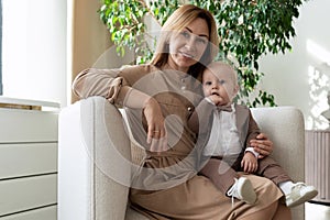 happy mother with her little son are sitting in an armchair in a bright room