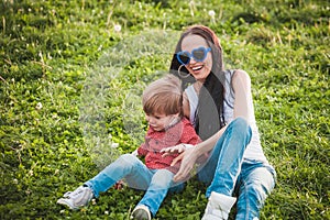 Happy mother with her little son sitting on grass in summer day