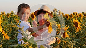 Happy mother and her son in a field playing with a sunflower at sunset.