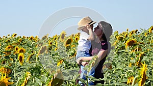 Happy mother and her son in a sunflower field at sunset. A young woman holds a baby in her arms.