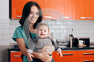 Happy Mother Holding Baby In Carrier in The Kitchen