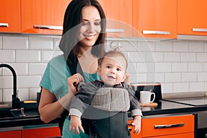 Happy Mother Holding Baby In Carrier in The Kitchen photo