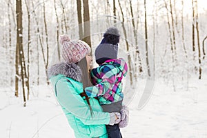 Happy mother holding baby girl on the walk in winter snowy forest