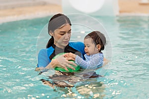 happy mother holding baby in her arms while playing ball in swimming pool