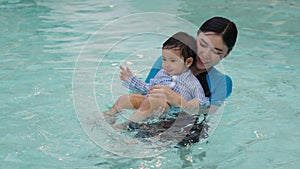 happy mother holding baby in her arms while playing water splashing in swimming pool