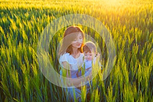 Happy mother holding baby smiling on wheat field in sunlight.