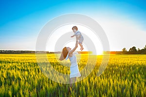 Happy mother holding baby smiling on wheat field in sunlight.