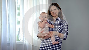 Happy mother holding cute baby girl in arms, smiling into camera, motherhood