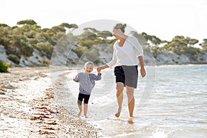 Happy mother holding hand of sweet blond little daughter walking together on sand at beach sea shore