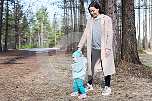 Happy mother holding hands of toddler baby while child trying to step by himself, learning to walk
