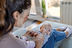 Happy mother holding and playing with infant girl on sofa at home