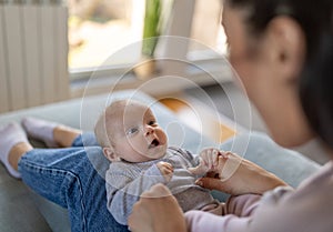 Happy mother holding and playing with infant girl on sofa at home