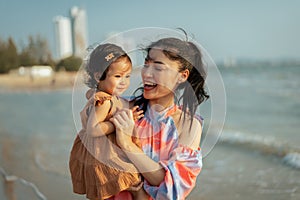 happy mother holding and talking toddler baby girl on sea beach